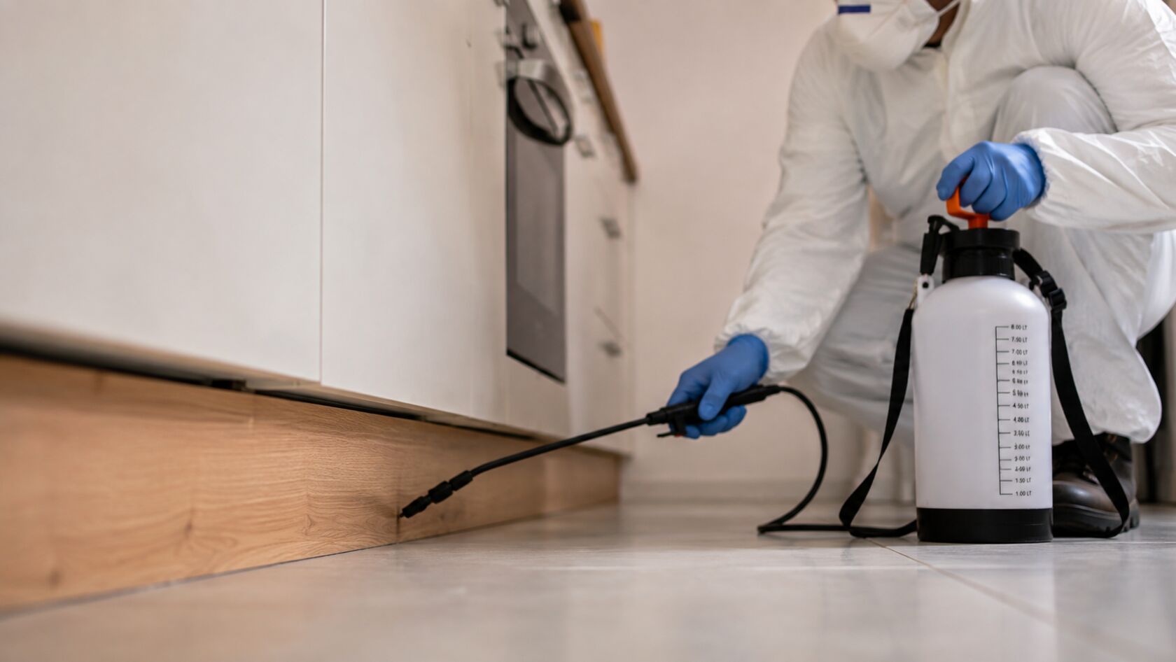 Technicien Nuisibles Secure pulvérisant un traitement anti-cafards le long d'une plinthe de cuisine